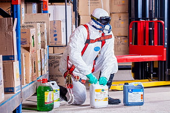 Industrial worker in protective gear handling chemicals in a warehouse environment. HD wallpaper