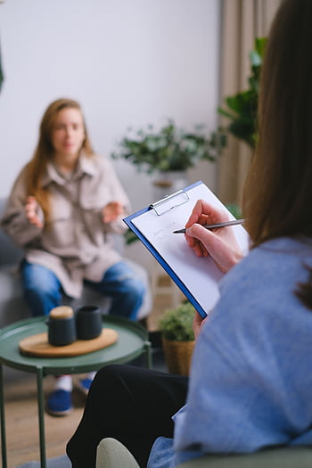 Focused therapy session with a counselor taking notes as client talks, highlighting mental health support. HD phone wallpaper