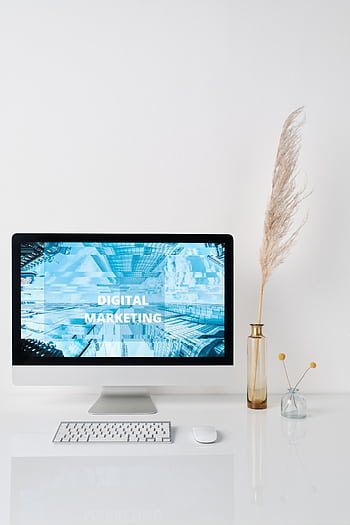 Modern workspace featuring a monitor displaying digital marketing graphics on a minimalist desk. HD phone wallpaper