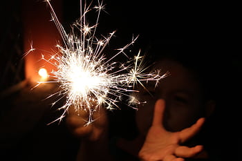 A child joyfully holds a bright sparkler in the dark, creating a magical moment. HD wallpaper