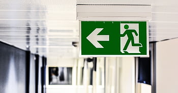 Green emergency exit sign with directional arrow in a hallway. HD wallpaper