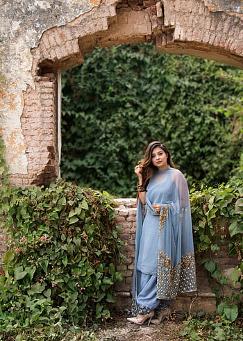 A woman in a beautiful blue traditional dress poses elegantly by ivy-covered ruins, exuding grace and charm. HD phone wallpaper