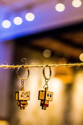 Close-up of two wooden keychain figures hanging on string with colorful bokeh lights in background. HD phone wallpaper