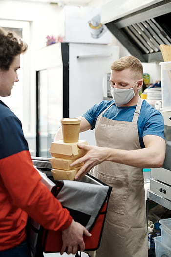 Masked worker packs takeaway food for delivery in restaurant kitchen. HD phone wallpaper