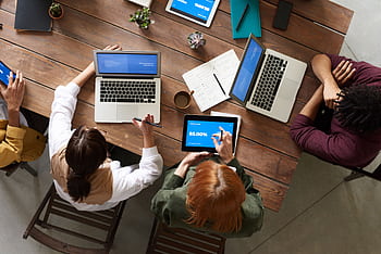 Team discussing strategies around a wooden table with laptops and tablets. HD wallpaper