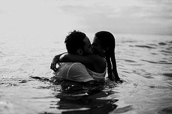 A romantic embrace and kiss in the ocean, captured in black and white. HD wallpaper