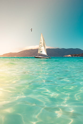 A sailboat glides across turquoise seas beneath a clear sky, ideal for tranquil travel and vacation scenes. HD phone wallpaper
