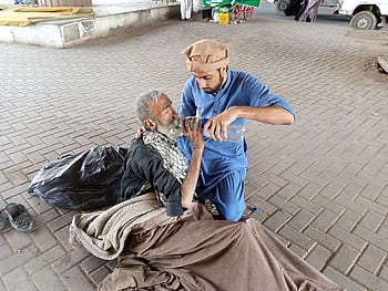 A young man helps a homeless senior by giving water outdoors in Karachi, Pakistan. HD wallpaper