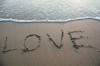 Love written in sand with ocean waves at the beach, evoking romance and tranquility. HD wallpaper