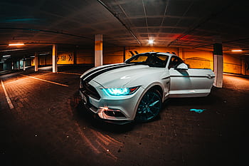 A striking white sports car with headlights on parked in an urban parking garage at night. HD wallpaper