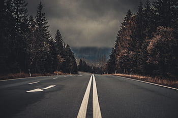 A moody highway through the forest in Harz, Germany, under dark clouds. HD wallpaper