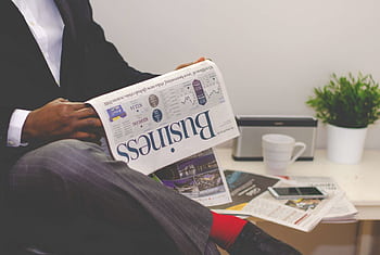Businessman reading a financial newspaper at a desk, highlighting finance and commerce theme. HD wallpaper