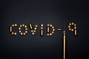 Artistic depiction of COVID-19 using pills and a syringe on a dark background, symbolizing medication. HD wallpaper