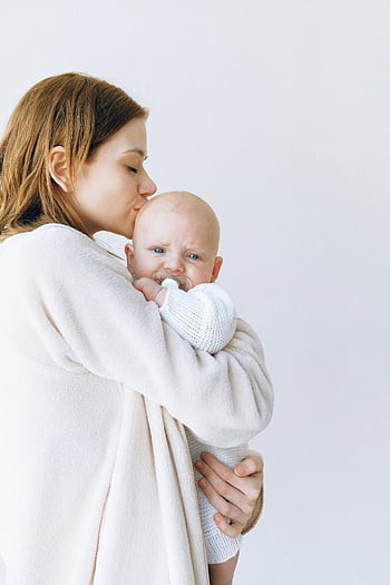 Loving mother gently kisses her calm baby wrapped in a warm sweater. HD phone wallpaper