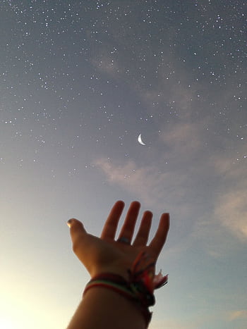 A hand reaches towards a crescent moon against a backdrop of a starry night sky. HD phone wallpaper