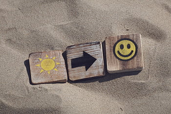 Wooden blocks with sun, arrow, and smiley emoticons on sand, evoking summer vibes. HD wallpaper