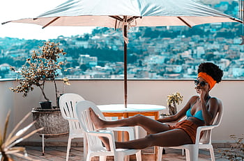 A woman enjoys leisure time on a terrace, lounging beneath a parasol during a sunny day. HD wallpaper