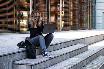 A woman working remotely on laptop outdoors, wearing casual attire in urban Leiden. HD wallpaper