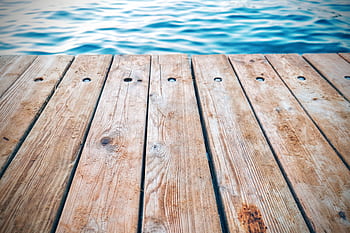 A detailed view of a rustic wooden pier with textured planks by calm blue water. Perfect for serene and nature themes. HD wallpaper