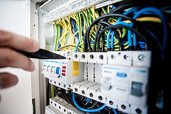 Hand of electrician working on a circuit breaker panel with colorful wires, ensuring safe electrical connections. HD wallpaper
