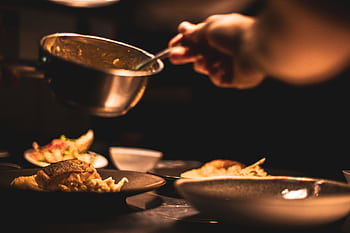 Gourmet dish being plated by a chef in a dimly lit restaurant's kitchen. HD wallpaper