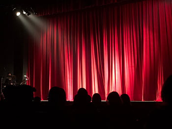 Dimly lit theater stage with red curtains and audience silhouettes under spotlights. HD wallpaper