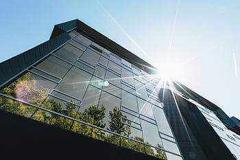 Low angle view of a modern skyscraper with reflections and sun flare, emphasizing contemporary architecture. HD wallpaper