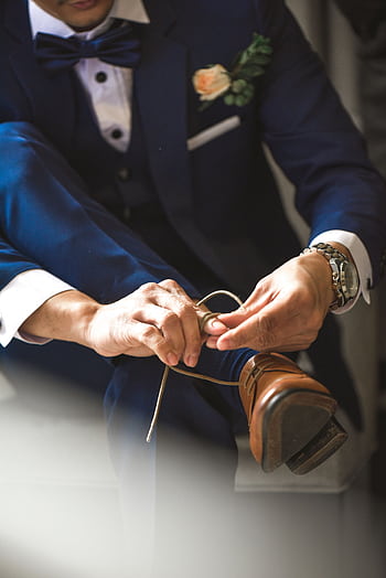 Close-up of a man in a suit tying his brown leather shoes, set indoors. HD phone wallpaper