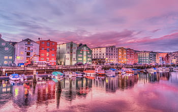 Vibrant waterfront scene with colorful buildings and boats reflecting in the water at sunset. HD wallpaper