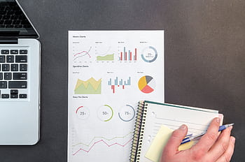 Overhead view of a business desk with charts and a laptop, ideal for data analysis concepts. HD wallpaper