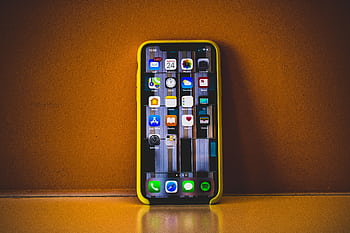 Close-up of a smart with a yellow case displaying various app icons, reflecting on a surface. HD wallpaper