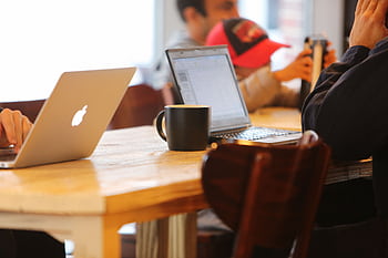 Group working in a cozy cafe with laptops and coffee mugs on a shared table. HD wallpaper