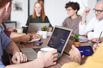 A diverse group of professionals collaborating with laptops and tablets in a modern office setting. HD wallpaper