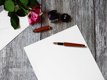 Flat lay of a rose, fountain pen, and paper on a rustic wooden table. HD wallpaper
