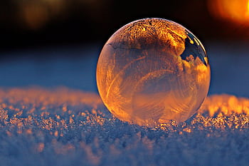 Close-up shot of a frozen bubble with warm reflections resting on a snowy surface at twilight. HD wallpaper