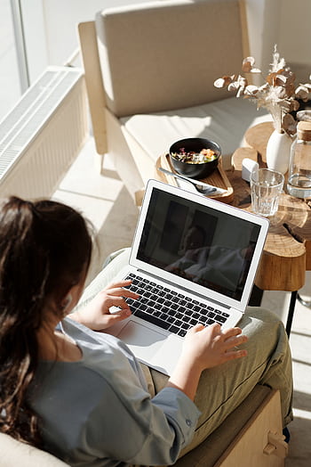 Woman enjoying remote work on a laptop in a cozy home setting with natural light. HD phone wallpaper