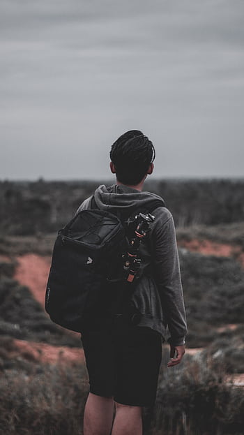 A young man with a backpack enjoys a quiet hike in a serene outdoor landscape. HD phone wallpaper