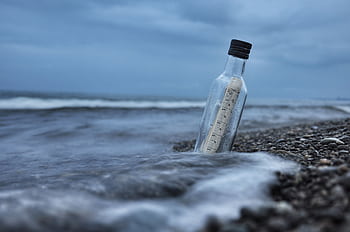 A serene of a message in a bottle on a rocky beach with waves crashing at dusk. HD wallpaper