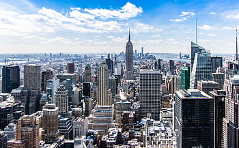A stunning aerial view of New York City's skyline featuring the iconic Empire State Building under a bright blue sky. HD wallpaper