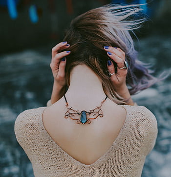 Glamorous young woman displaying a stylish gemstone necklace outdoors, posing with hands on head. HD phone wallpaper