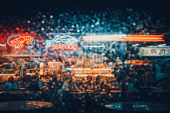Explore the neon-lit ambiance of a bustling seafood market in Kuching at night, captured through a rain-splattered lens. HD wallpaper