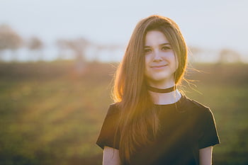 Portrait of a smiling young woman outdoors in a sunlit field, wearing a black choker. HD wallpaper