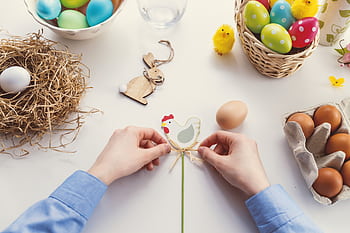 Hands arranging Easter decorations on a table with colorful eggs and festive decor. HD wallpaper