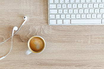 A minimalist desk featuring a keyboard, coffee cup, and ears on a wooden surface. HD wallpaper