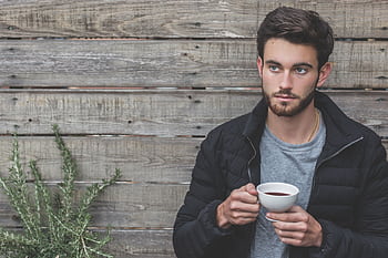 A contemplative young man enjoying tea against a rustic wooden backdrop. HD wallpaper