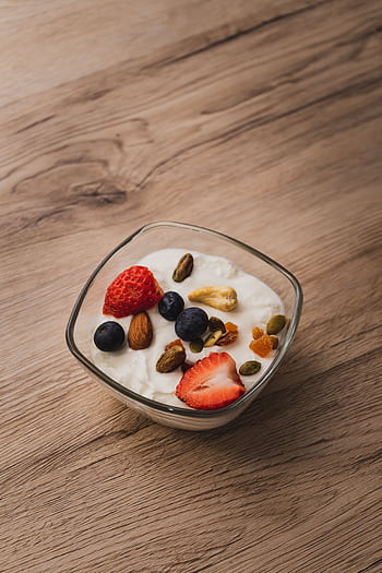 A bowl of yogurt topped with fresh strawberries, blueberries, and assorted nuts on a wooden table. HD phone wallpaper