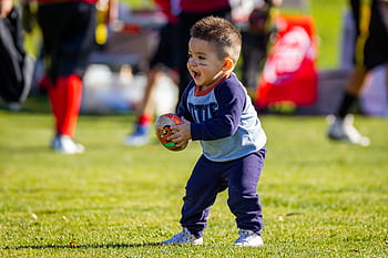 Joyful toddler playing with a football on a sunny day outdoors, dressed in casual clothes. HD wallpaper