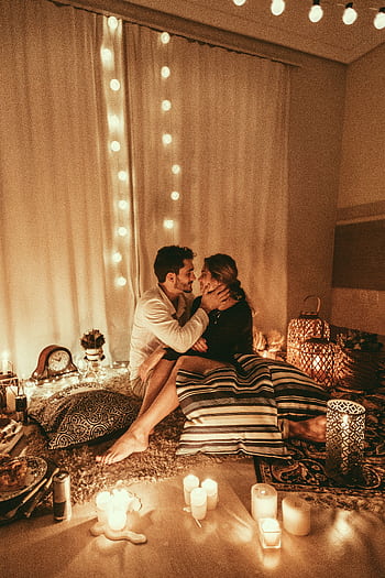 Couple embracing in a romantic candlelit room adorned with string lights. HD phone wallpaper