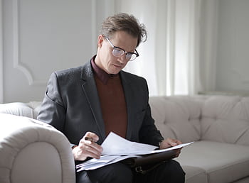 Elegant businessman in a suit reading important documents on a sofa indoors. HD wallpaper