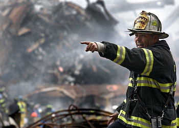 A firefighter in action at a disaster scene, directing rescue operations amidst smoke and debris. HD wallpaper